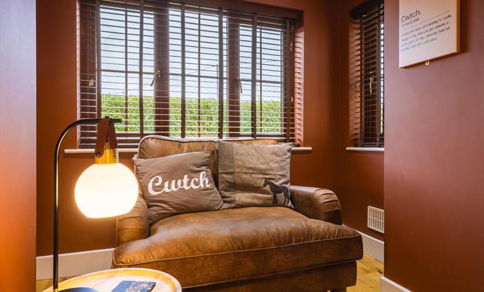 Large, two person Cwtch cuddle chair in a recess within the living room with Cwtch cushion and Cwtch sign and coffee table with reading lamp.